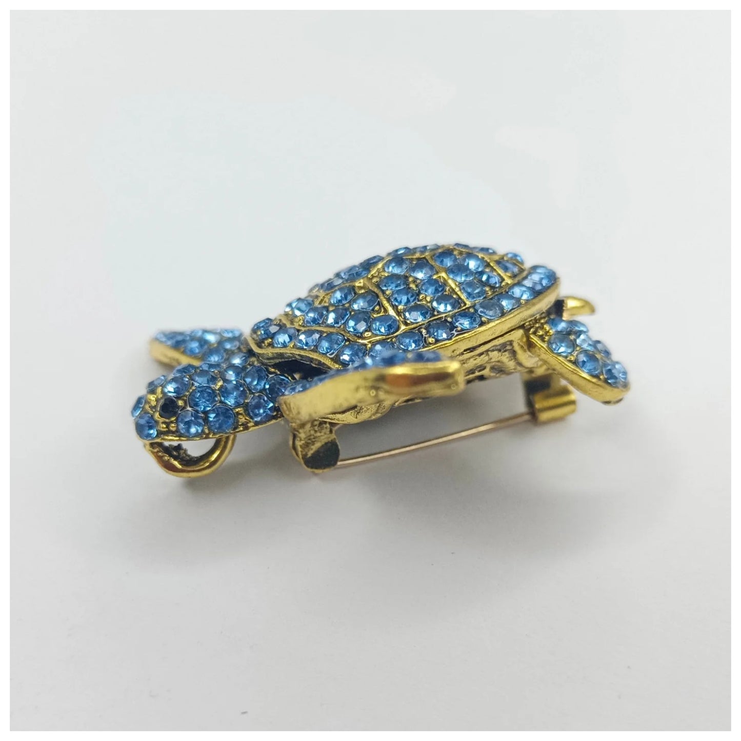 Gold turtle-shaped brooch with blue gemstones on a white background
