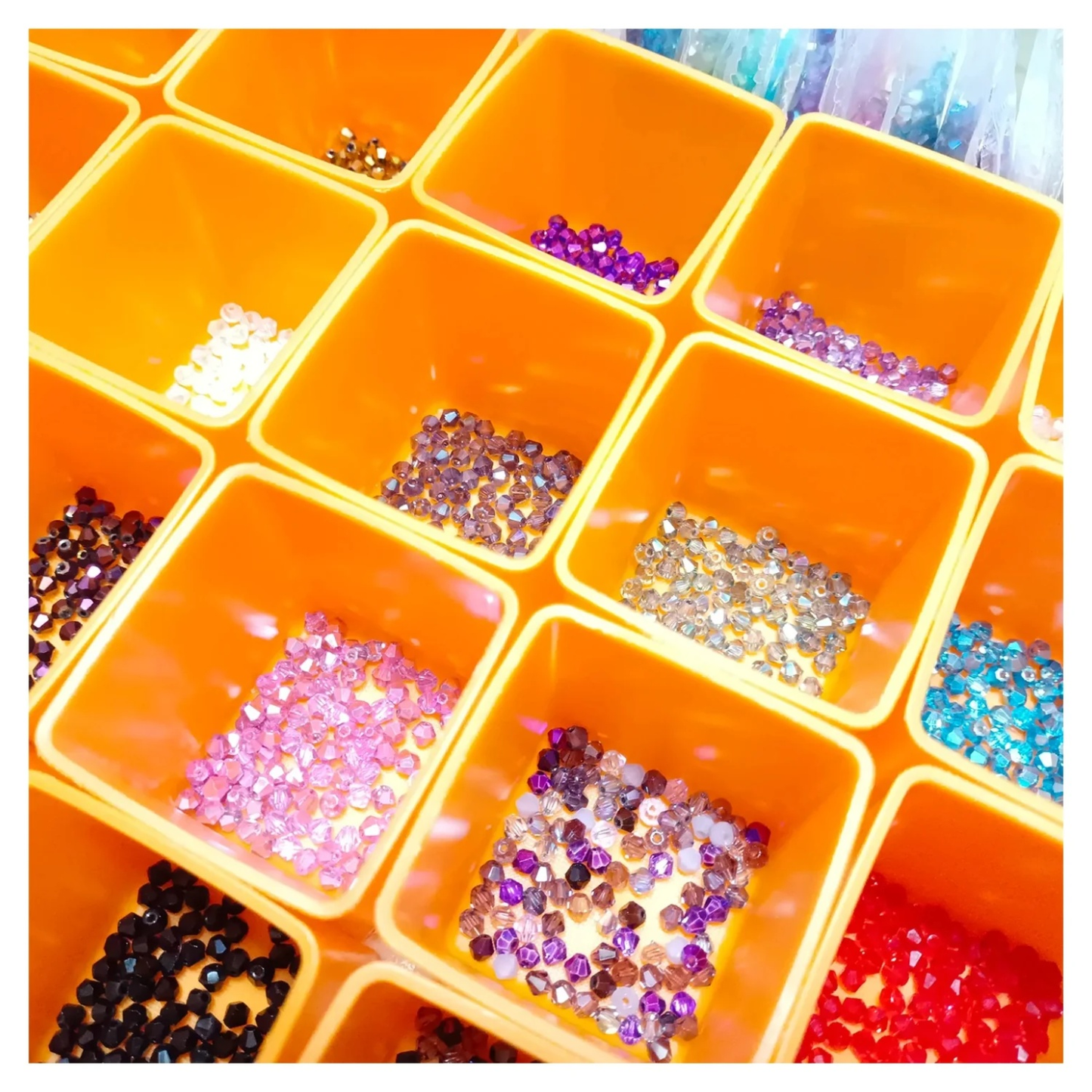 Orange container with compartments filled with various colored beads and sequins on a white background