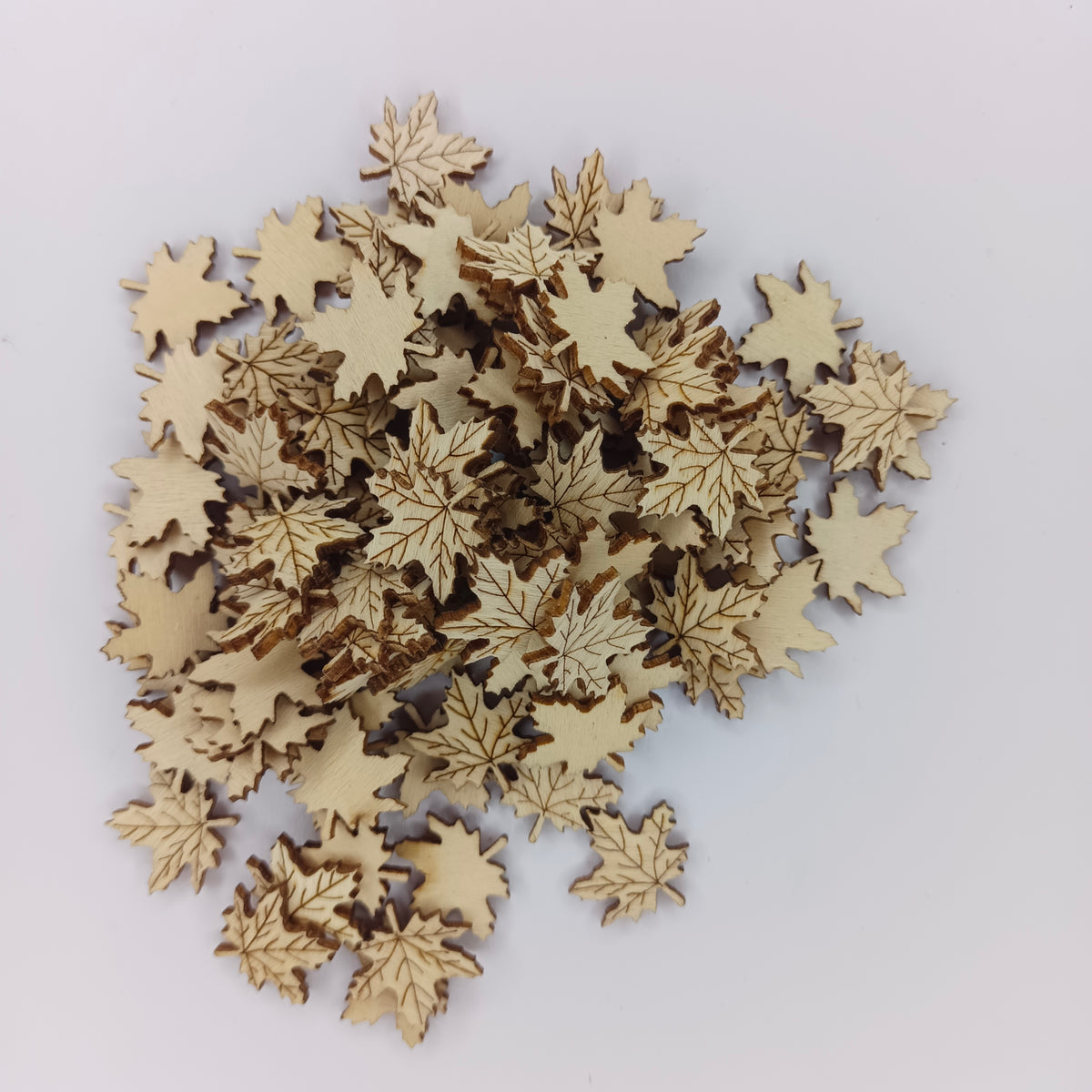 A pile of small laser-cut wooden maple leaf embellishments in a light natural wood tone, arranged on a plain white background.