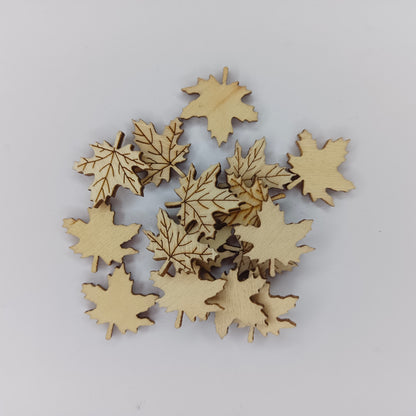 A pile of small laser-cut maple leaf embellishments made of natural light wood, arranged on a plain light gray background.