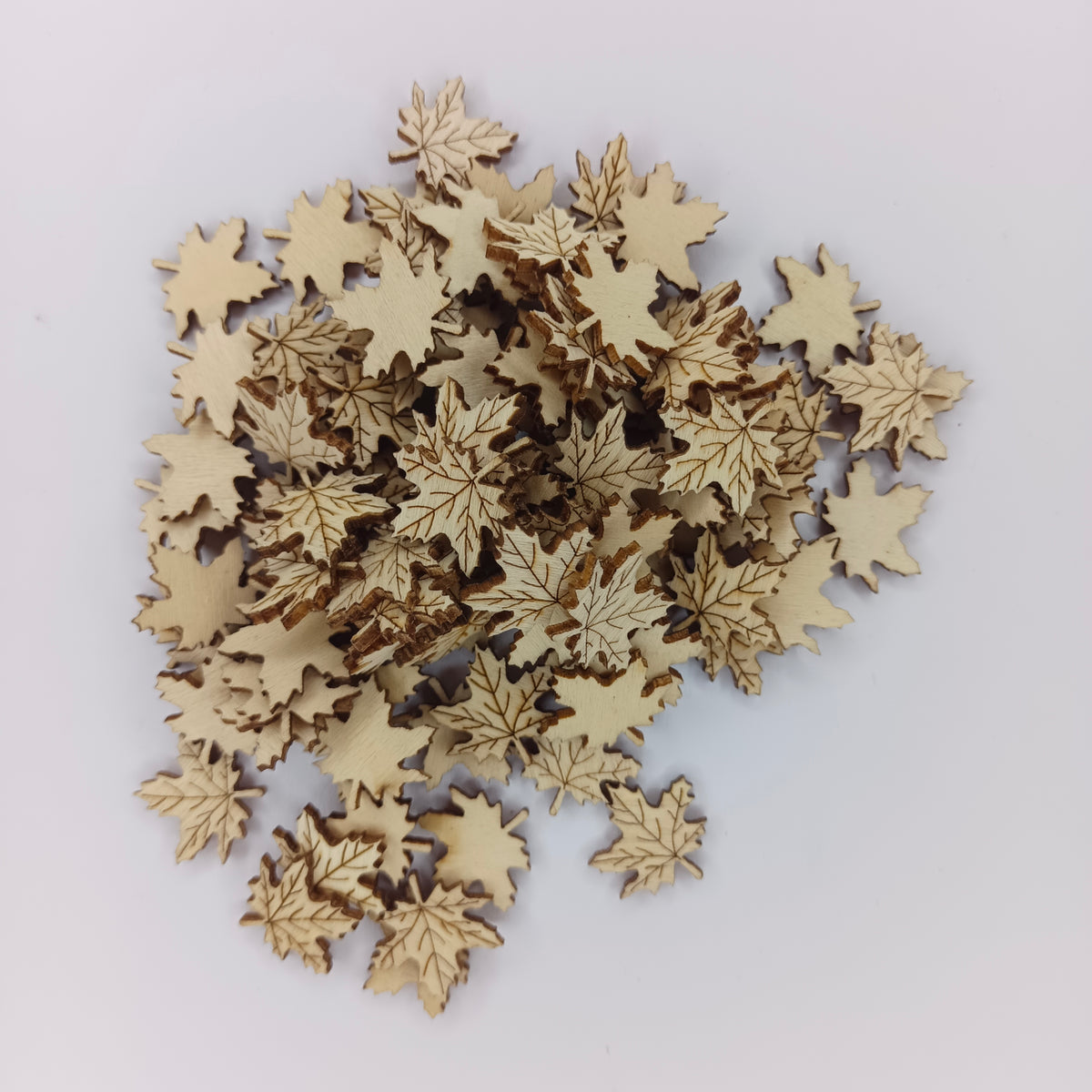 A pile of small laser-cut wooden maple leaf embellishments in a natural light wood tone, arranged on a plain white background.