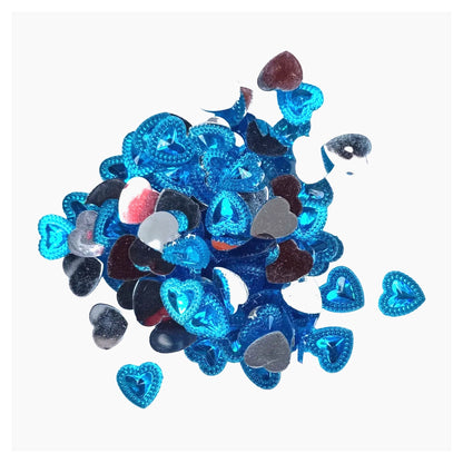 A pile of small heart-shaped rhinestones in metallic blue, silver, black, and white, arranged on a plain light gray background.