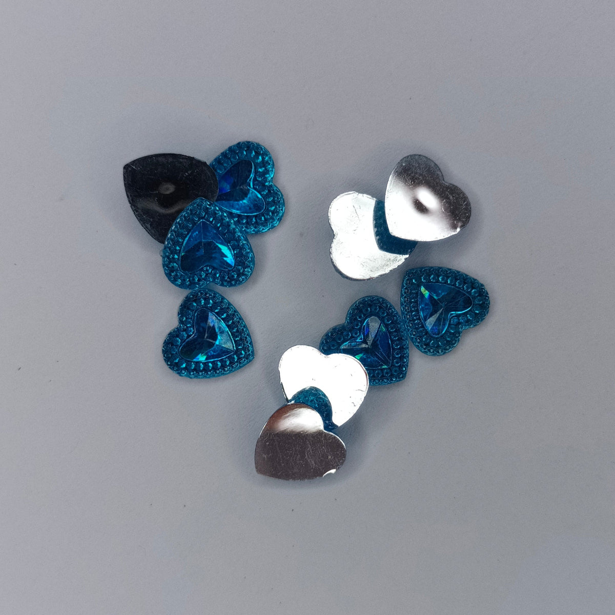 A group of small heart-shaped sequins in metallic silver, dark blue, and black, arranged on a plain gray background.
