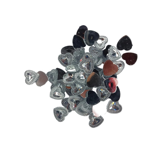 A pile of small heart-shaped rhinestone embellishments in silver, black, and rose gold, arranged on a white background.