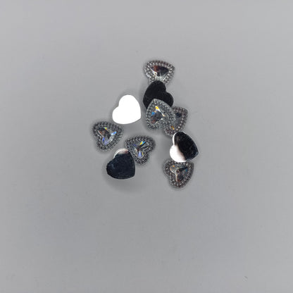 A set of small heart-shaped rhinestone embellishments in silver, black, and iridescent white, arranged on a plain light gray background.