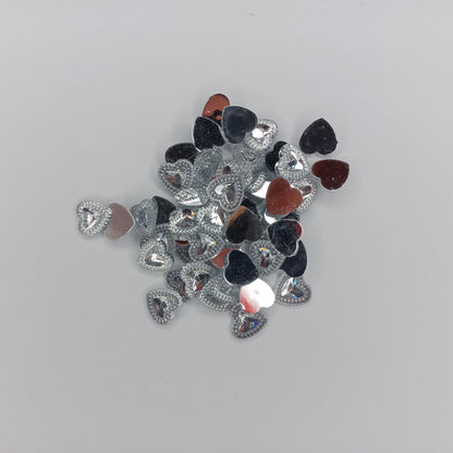 A pile of small heart-shaped rhinestones in silver, black, and reddish-brown, arranged on a plain light gray background.