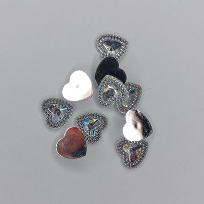 A small cluster of heart-shaped reflective embellishments or charms in silver, black, white, and red, arranged on a plain light gray background.