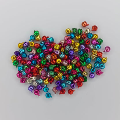 A pile of small metallic bell-shaped beads in assorted bright colors, including red, blue, green, yellow, pink, and purple, arranged on a plain light gray background.