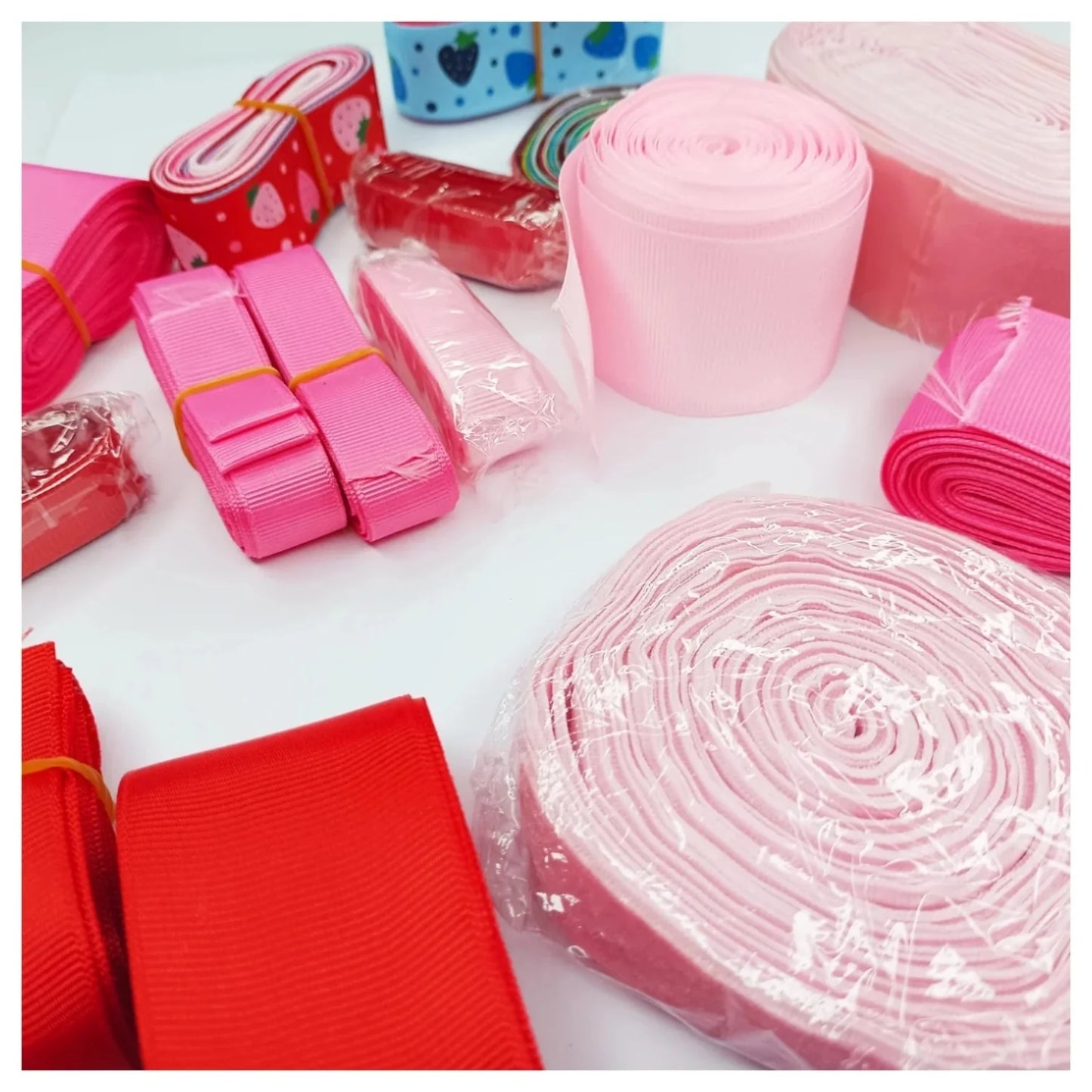 Assorted rolls of pink and red ribbons on a white surface