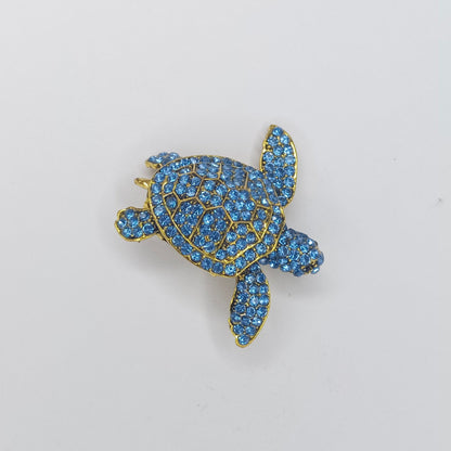 Blue turtle-shaped brooch with gold accents on a light gray background