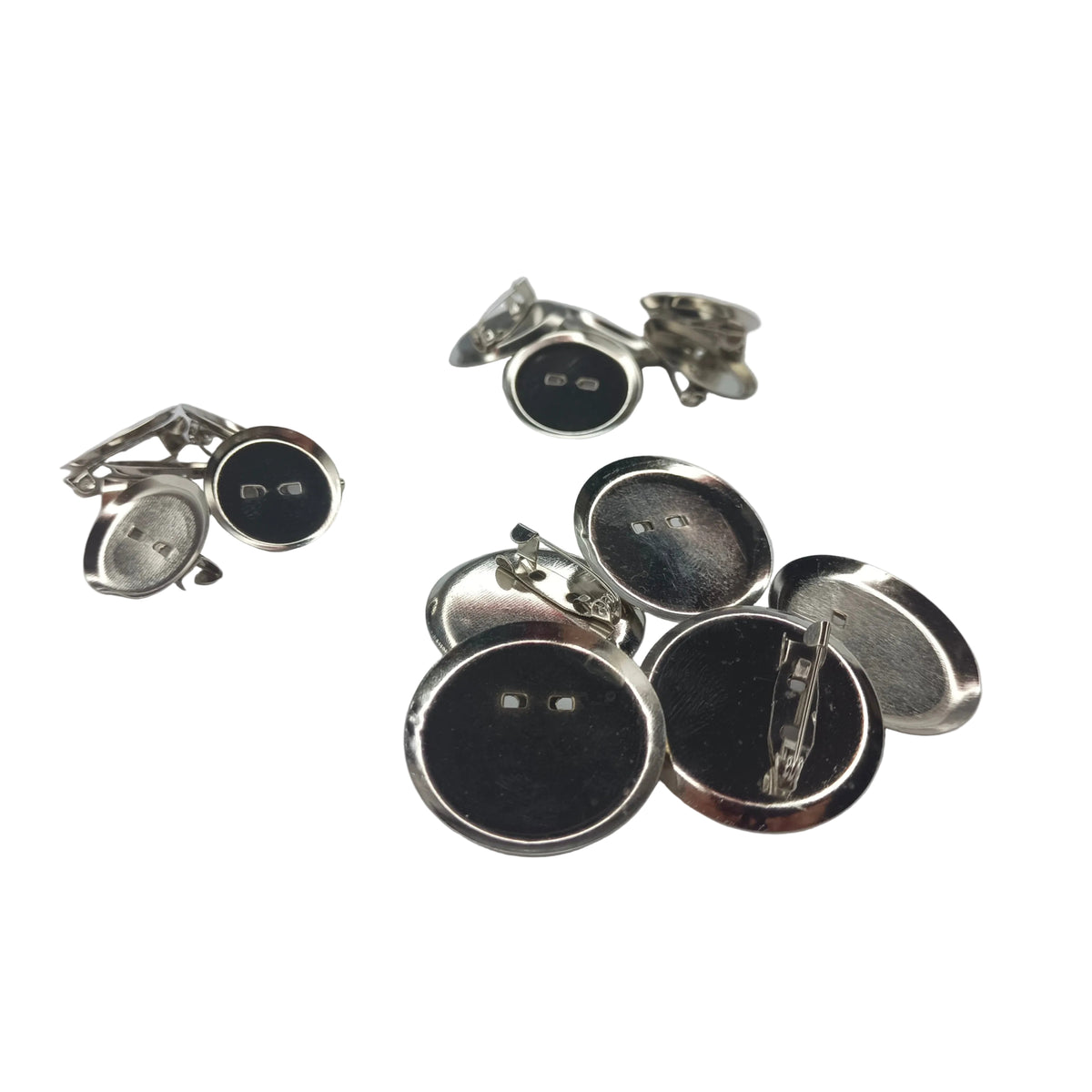 Several small round metallic pin-back cabochon holders, mostly shown from the back on a light gray background. The buttons have silver-toned metal backs.