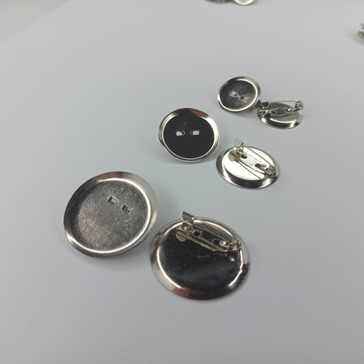Six silver metal pinback buttons shown from both front and back on a light gray background.