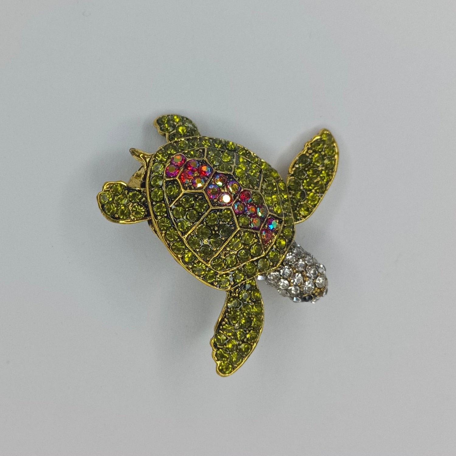 Decorative turtle brooch with gemstones on a gray background