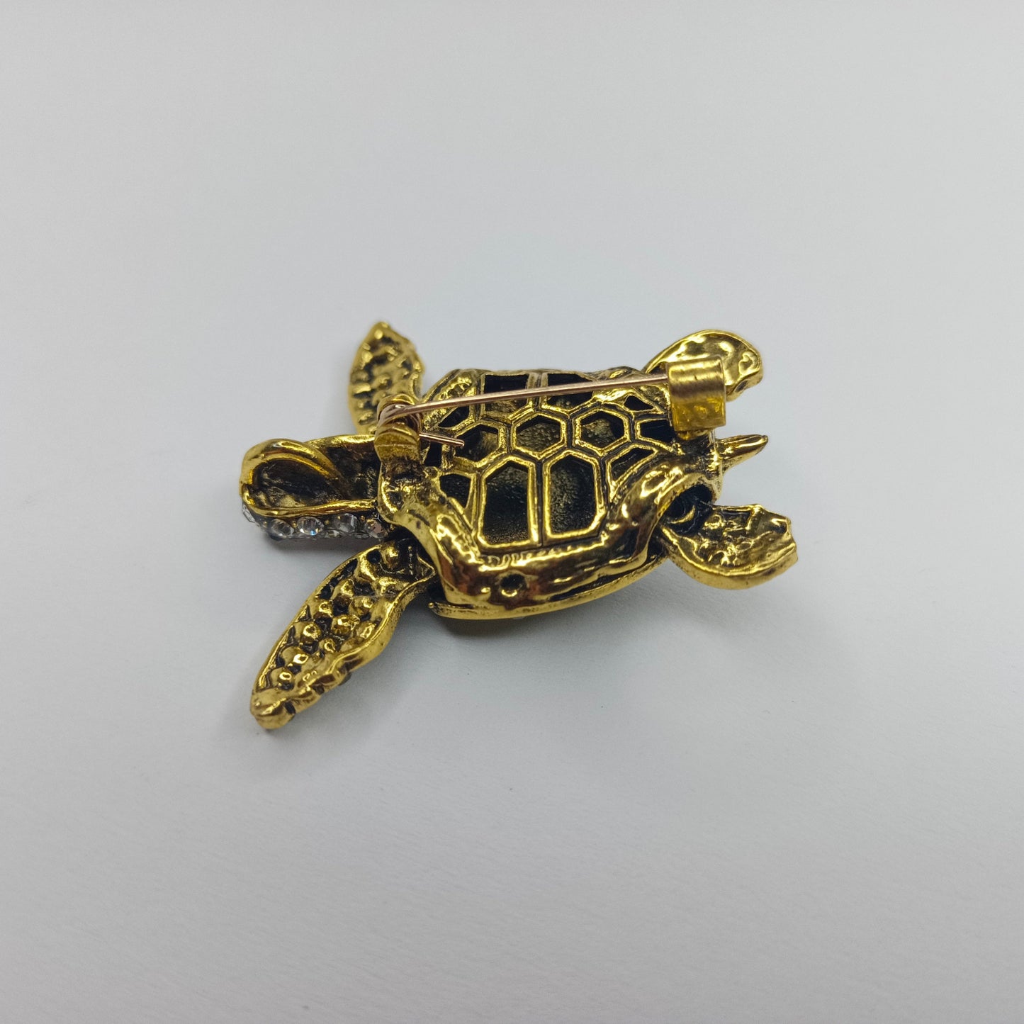 Gold turtle-shaped brooch on a light gray background