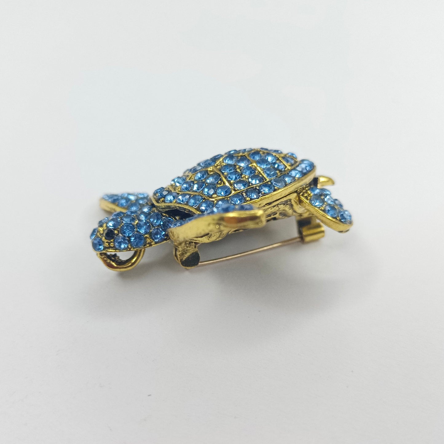 Gold turtle-shaped brooch with blue gemstones on a white background