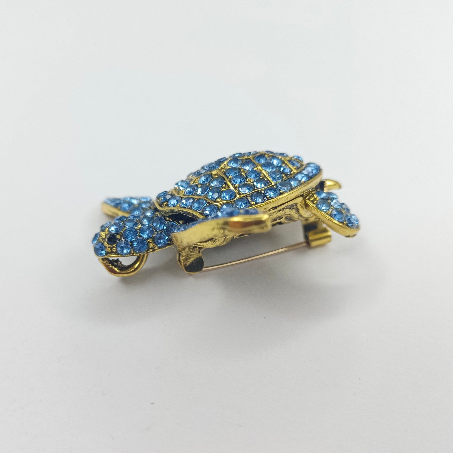 Gold turtle-shaped brooch with blue gemstones on a white background