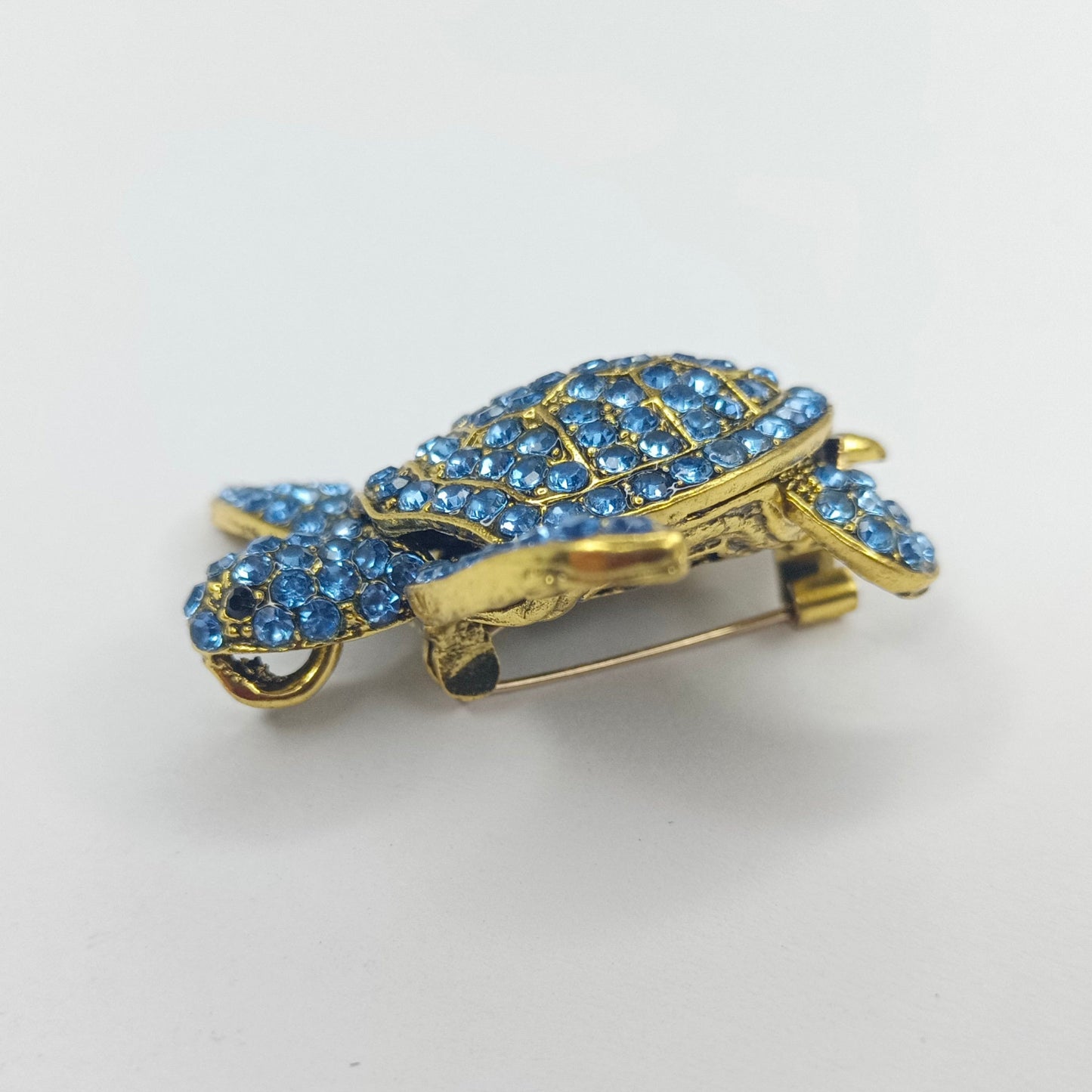 Gold turtle-shaped brooch with blue gemstones on a white background