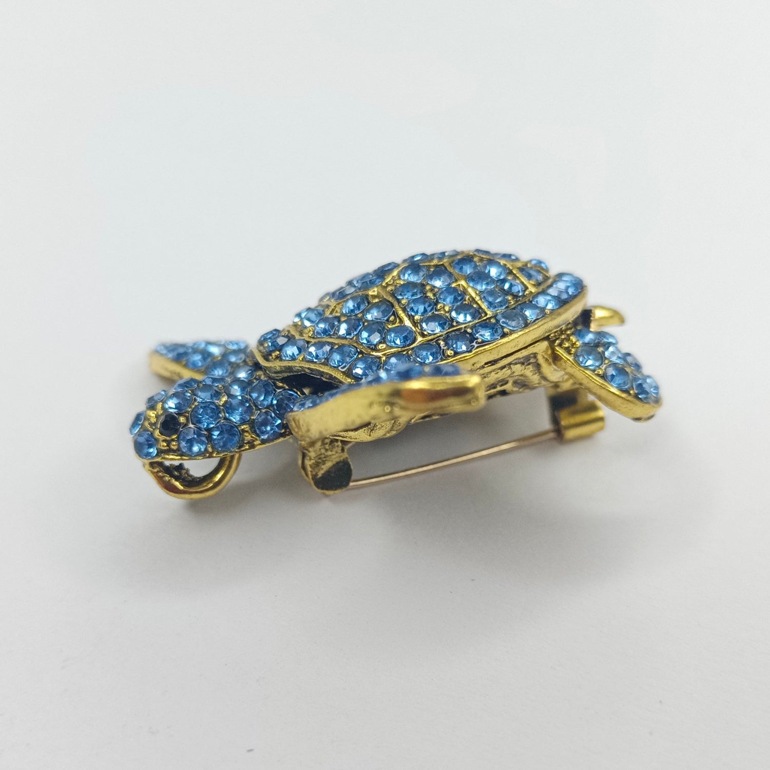 Gold turtle-shaped brooch with blue gemstones on a white background