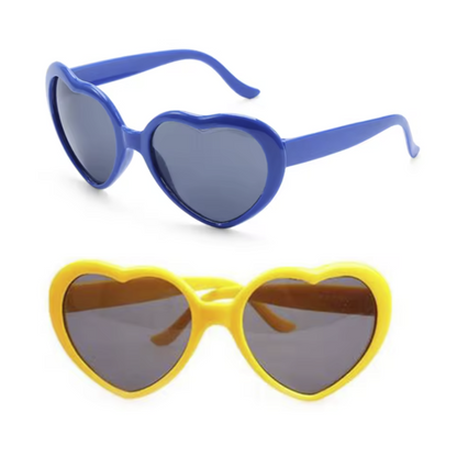 Blue and yellow heart-shaped novelty sunglasses on a white background that make a Heart-Shaped rainbows in the surrounding light as you look through them