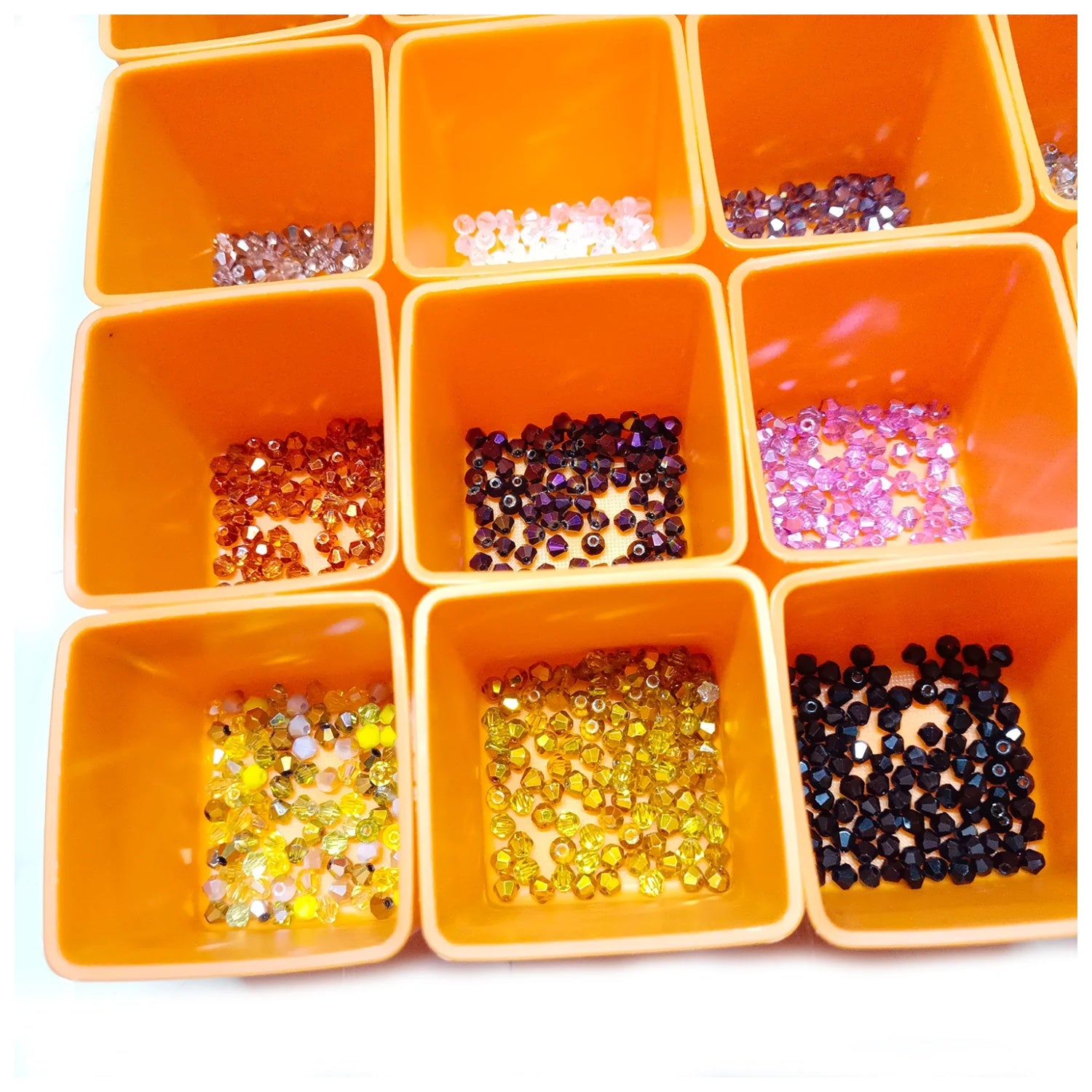 Orange container with compartments filled with various colored beads and sequins on a white background