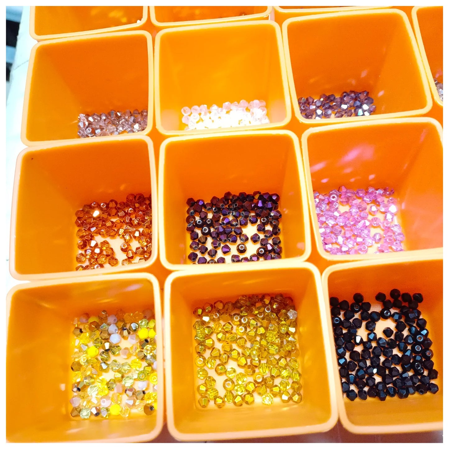 Orange container with compartments filled with various colored beads and sequins on a white background