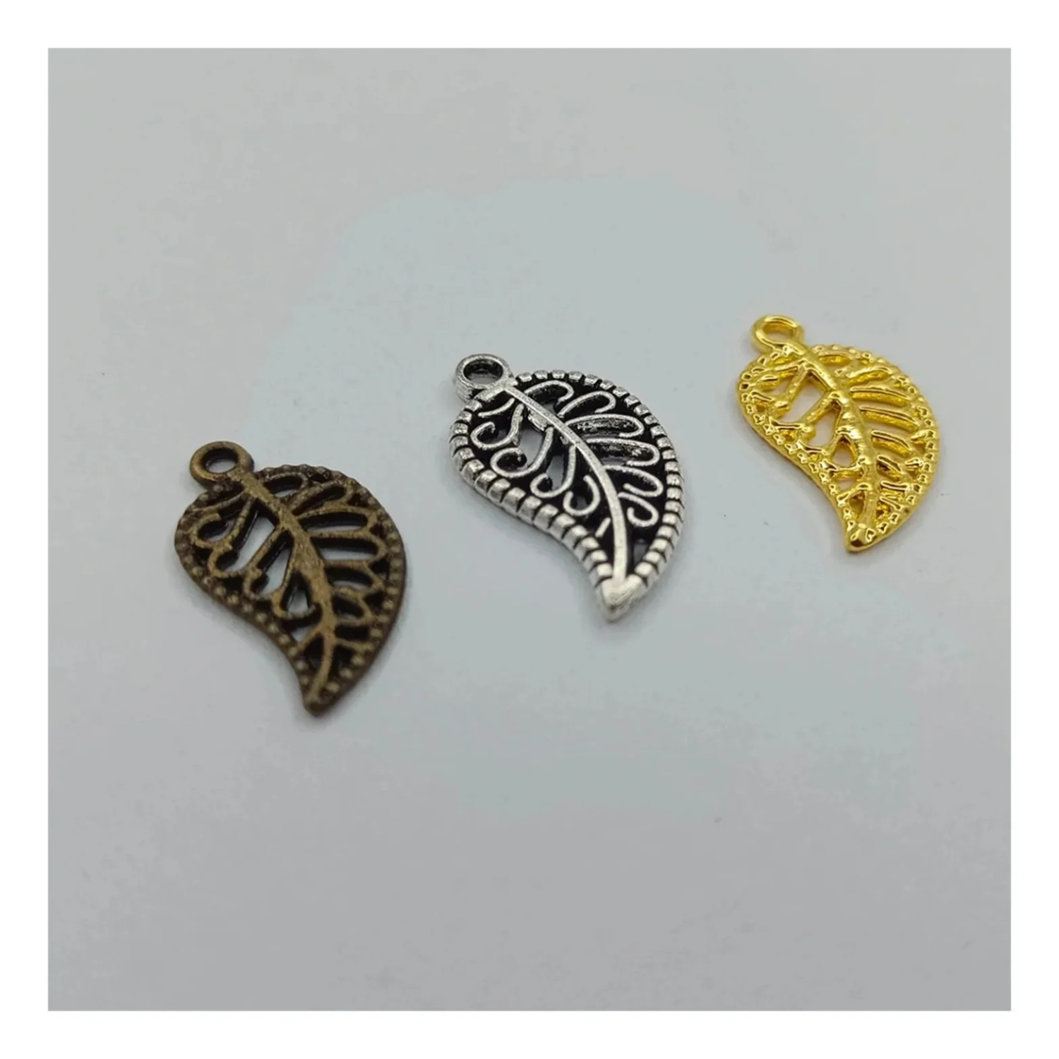 A collection of leaf-shaped charms in gold and silver colors with intricate patterns, intended for use in crafting jewelry such as bracelets and necklaces.