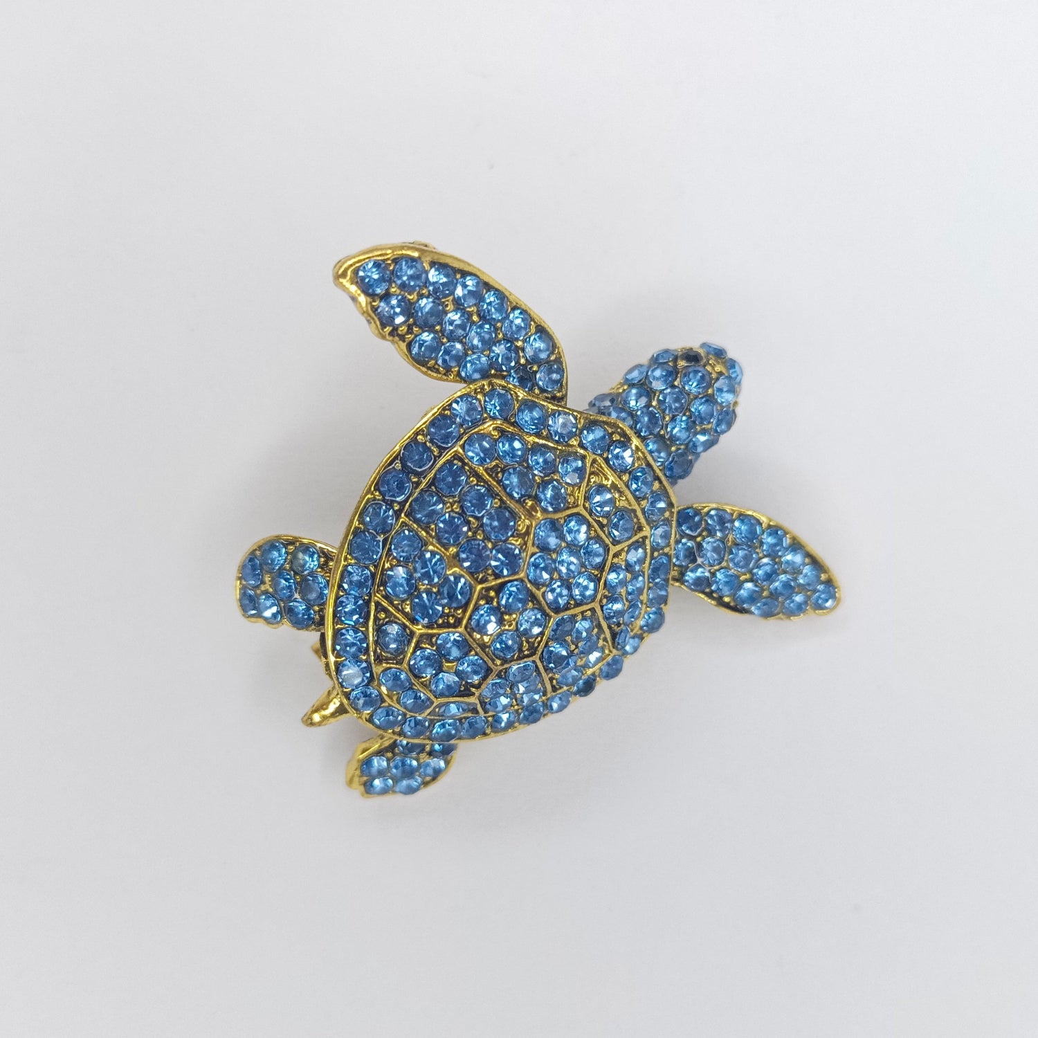 Tortoise-shaped brooch with blue gemstones on a light gray background