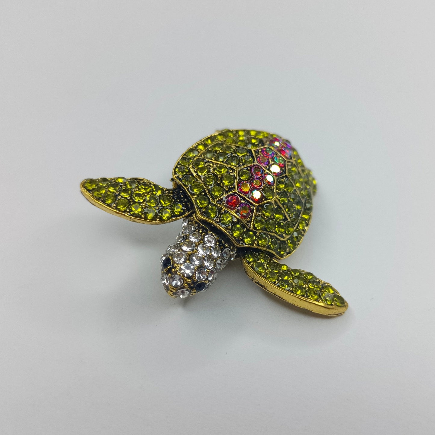 Tortoise-shaped brooch with gemstones on a light gray background