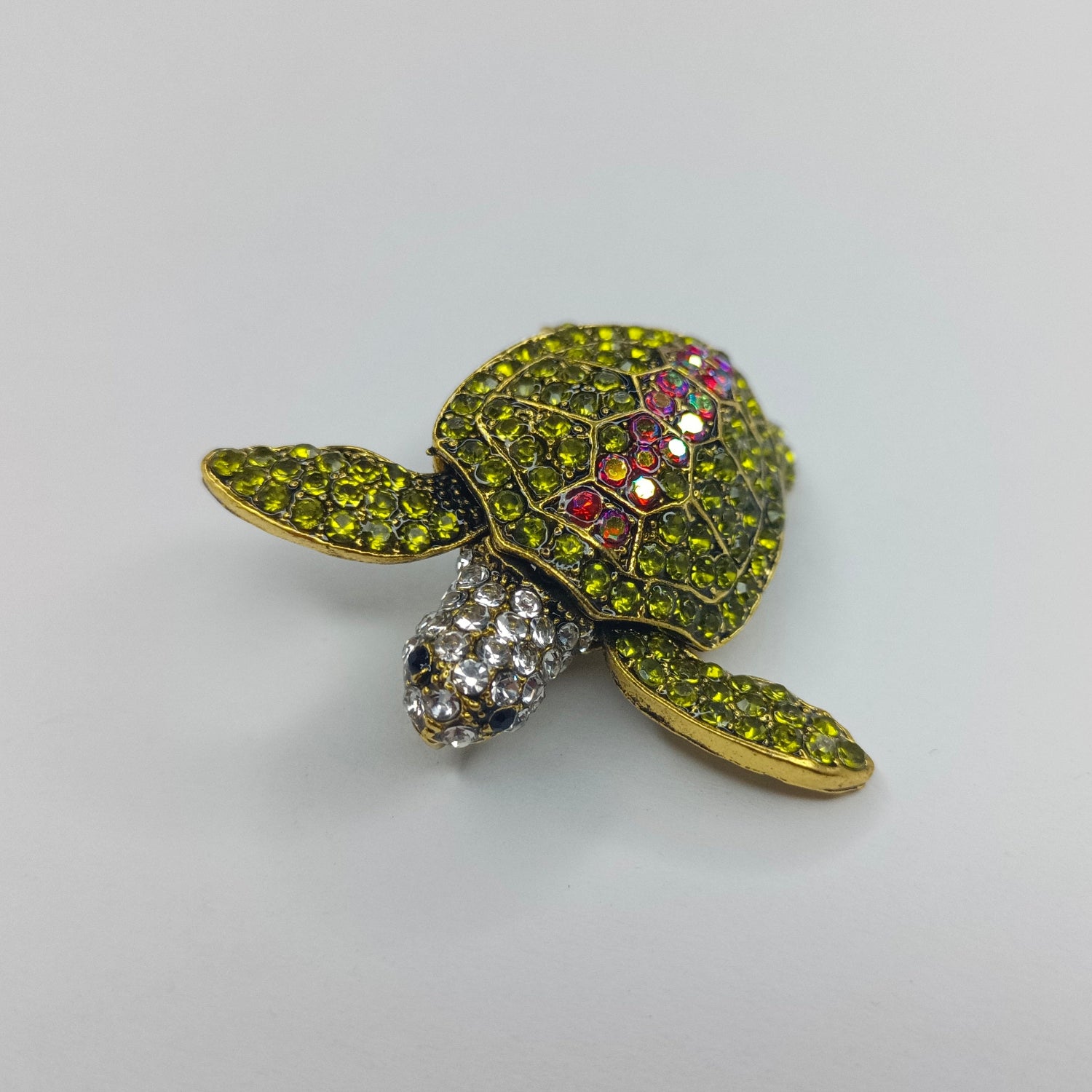 Tortoise-shaped brooch with gemstones on a light gray background