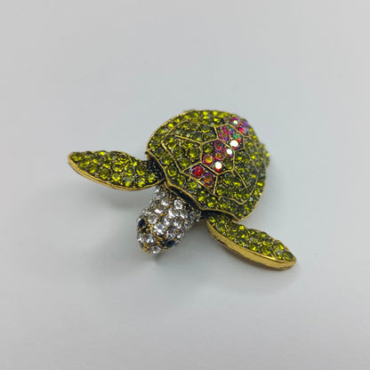 Tortoise-shaped brooch with gemstones on a light gray background