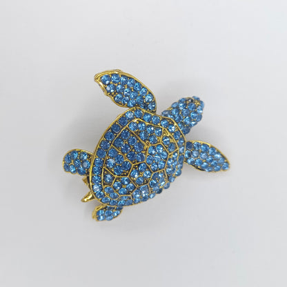 Turtle-shaped brooch with blue gemstones on a white background