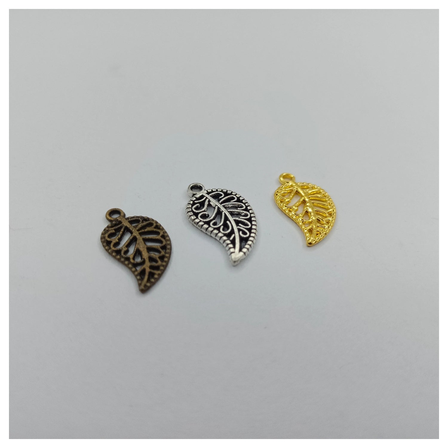 Three leaf-shaped charms in bronze, silver, and gold on a gray background