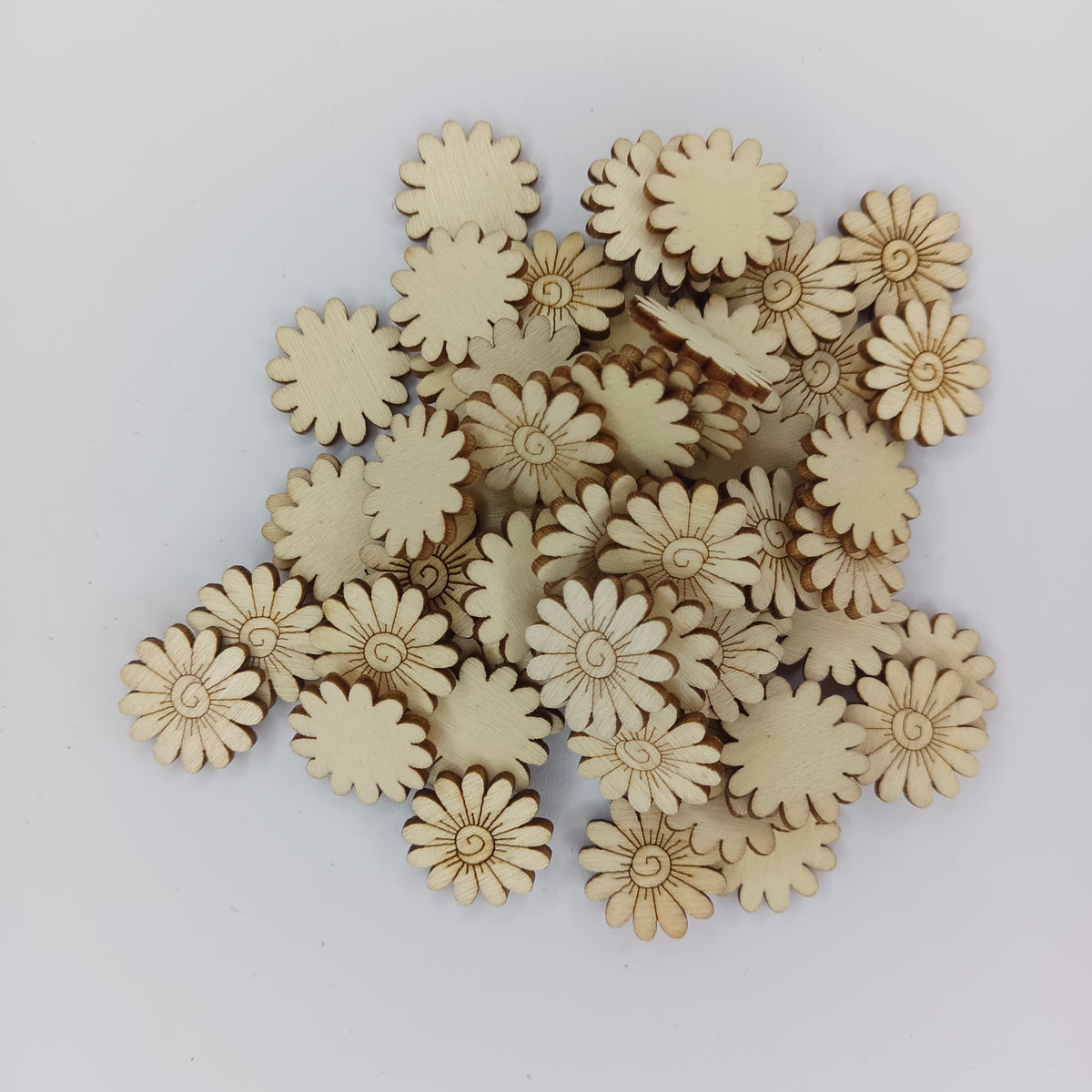 A pile of small natural wood daisy-shaped craft embellishments on a plain light gray background.
