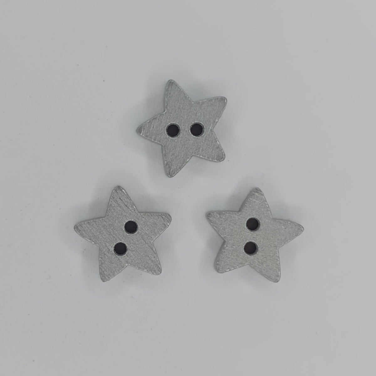 Three small gray wooden star-shaped buttons with two holes, arranged in a triangle on a plain white background.